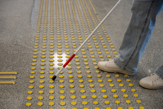 A blind woman walks on tactile paving. Close-up of her feet and a walking stick.