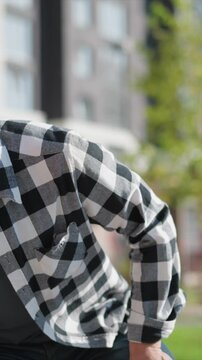 Close up of young man wearing black and white checkered flannel shirt sitting outdoors in bright daylight. subject casual attire includes blue jeans visible at bottom frame with soft natural