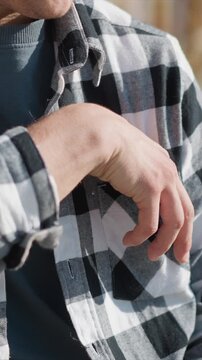 Close up of man wearing black and white checkered flannel shirt reaching into his pocket to retrieve blister packs. fabric texture details are visible under natural light with soft shadows