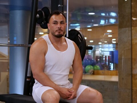 Sweaty young man resting on gym bench, looking directly at camera after workout session.