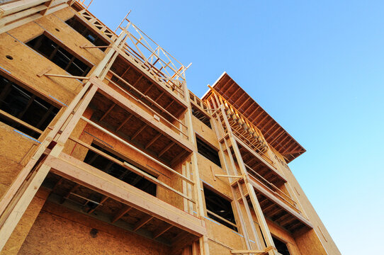 Detail of a multistory apartment building under construction showing wood framing, sheathing and structural openings, illustrating multifamily housing development and carpentry