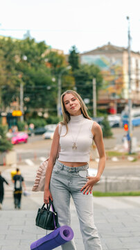 Young woman with yoga mat and handbag walking on city street stairs