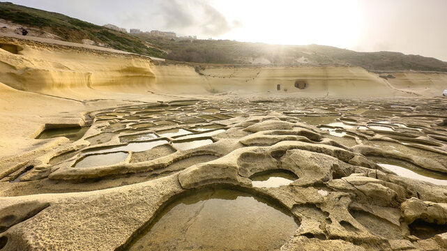 Zebbug, Gozo, Malta - December 7, 2022: Rock-cut salt pans and caves carved into the limestone cliffs of the Xwejni coast, shrouded in sea mist