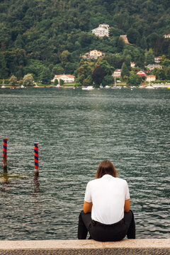Un homme assis de dos face &agrave; un lac. Homme r&eacute;fl&eacute;chissant face au Lac Majeur. Solitude en vacances. Nostalgie et tristesse humaine