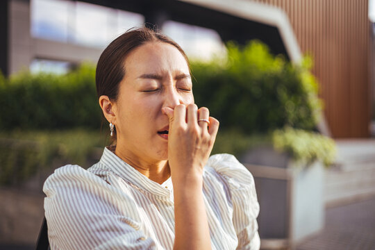 Young Woman Pinching Her Nose and Sneezing Outdoors From Allergy or Bad Odor