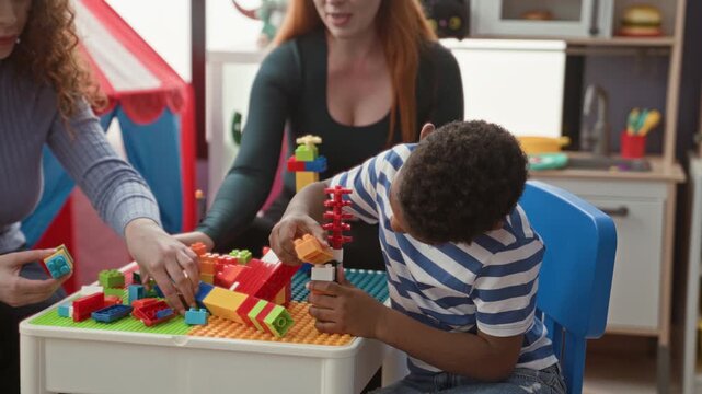 Woman teacher guides boy stacking colorful blocks with hands at table inside building; concentration cooperation.