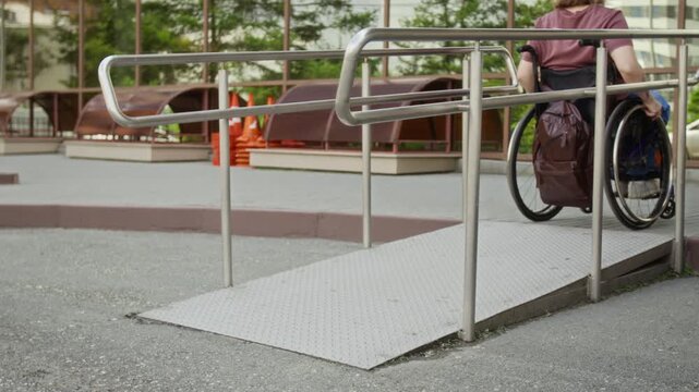 Young adult Caucasian woman with disability pushing wheelchair up outdoor metal ramp. Footage suits commercial projects on social diversity and urban accessibility