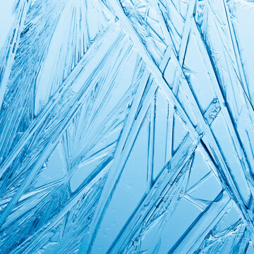 Ice frozen in intricate patterns of delicate crystals in blue and teal. Detailed textures of real unique patterned crystal formations. Sparkling window frost or icy cold winter frosting background.