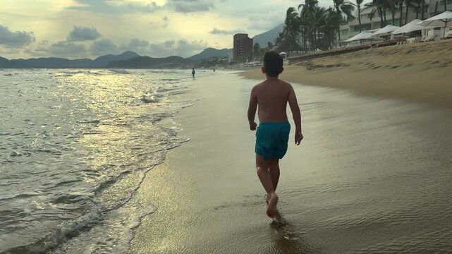 un ni&ntilde;o tranquilo disfrutando de su dia caminando feliz por la playa en la orilla del mar caminando por la arena mojada con un cielo hermoso atardecer al aire libre en la naturaleza majestuosa