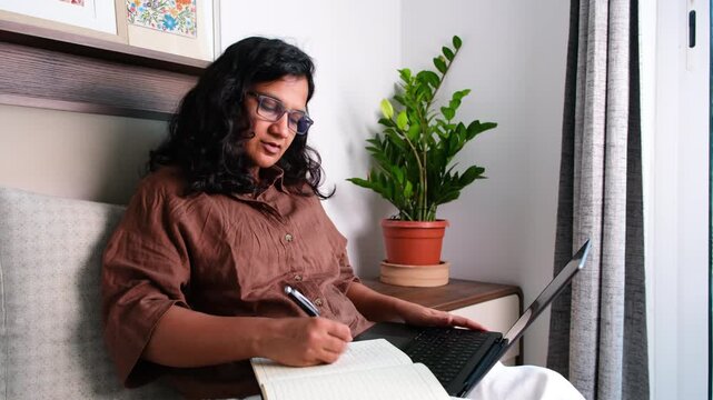Woman taking notes while watching online course on laptop at home, e learning, remote education, online study, skill development and digital learning concept