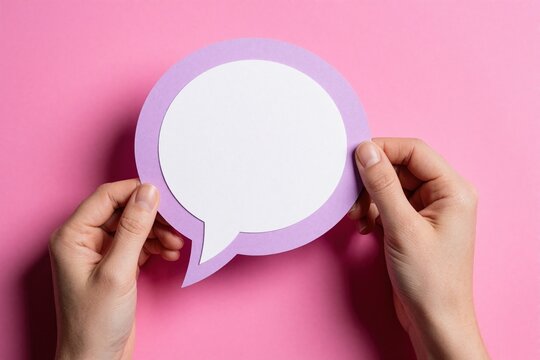 Hands hold large purple speech bubble paper over pink background. Person displays blank chat icon for message text. Minimalist concept for communication, social media feedback, empty comment space.