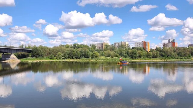 View of a small tourist ferry flying the Polish flag as it cruises along the calm waters of the Vistula River beneath a beautiful summer sky in Warsaw, Poland.