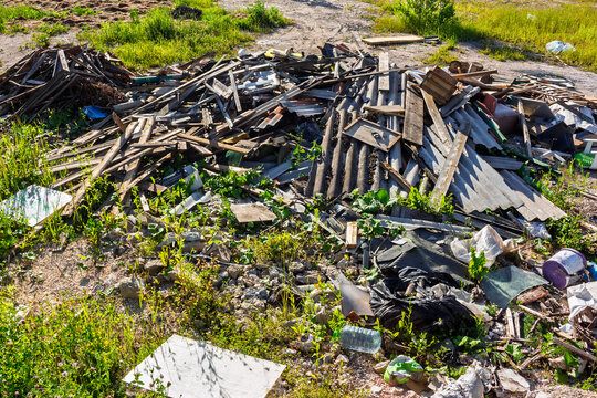 Large heap of discarded construction debris, broken wooden boards, corrugated metal sheets, and assorted waste scattered on grassy ground in an open field, environmental pollution scene