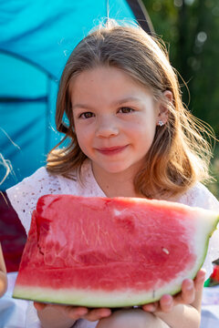 Young girl smiling while holding a large slice of watermelon outdoors during summer picnic