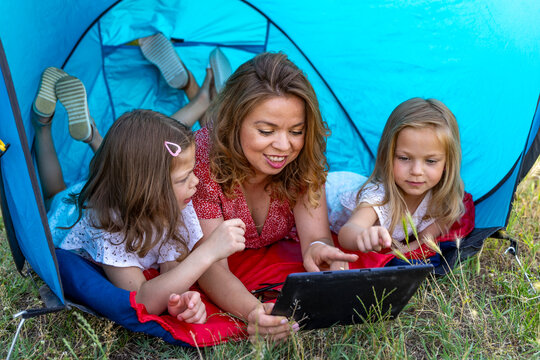 Family lying in a tent, bonding and using a tablet during leisure time outdoors