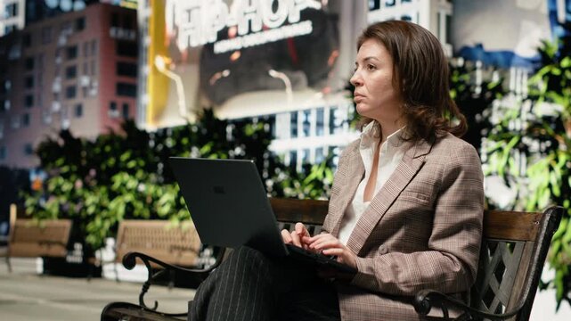 Businesswoman typing on laptop keyboard while working on park bench