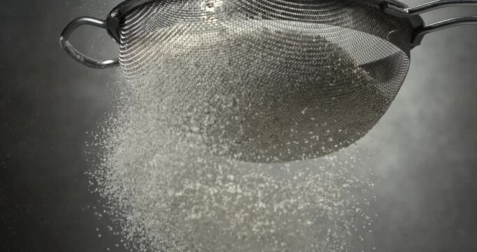 Flour sifts through a sieve creating soft powder cloud in slow motion