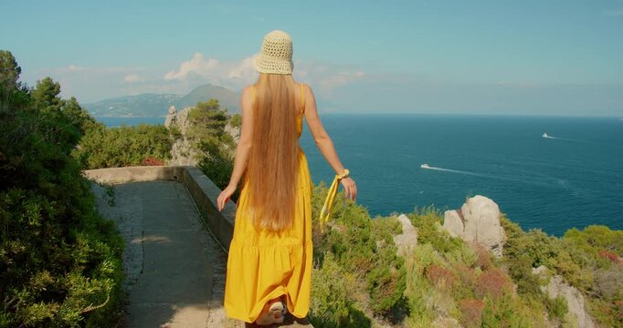 Woman walks a sunny coastal path above the blue Mediterranean sea on Capri in Italy