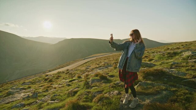 Person taking a selfie on a mountain with a sunset in the background near a winding road