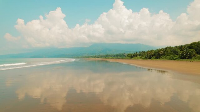 Fluffy clouds reflect on wet sand beach in Marino Ballena National Park Costa Rica