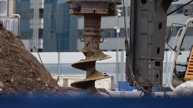 Heavy drilling equipment with auger working on soil at an urban construction site, capturing foundation preparation, ground engineering and early stage building construction