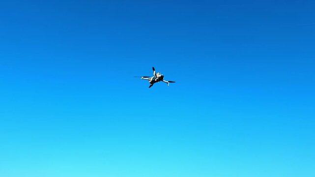 Drone flies in clear blue sky. A drone hovers high above in a bright blue sky during daylight. It captures images from above.