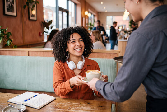 Friendly Waitress Serving Hot Latte to Smiling Female Customer Sitting at Cafe Table