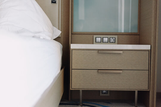 Bed and minimalist nightstand beside a clean bed with drawers and wall outlets in a modern hotel style bedroom scene, soft lighting, uncluttered decor