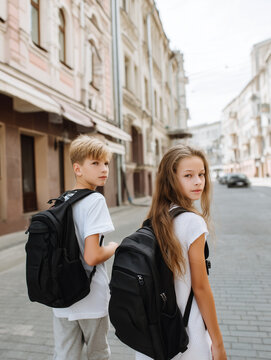 Zwei Sch&uuml;ler mit Rucks&auml;cken auf dem Weg durch die Stadt blicken zur&uuml;ck. Schulweg, Freundschaft, Jugend, Bildung, Schulalltag, Teenager und moderner urbaner Lifestyle.