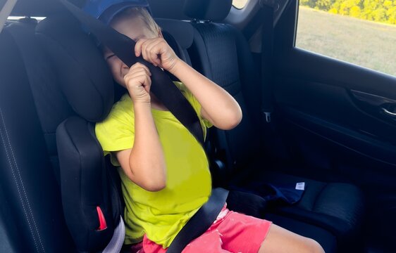 child plays with seatbelt in car interior, side view, playful scene, family travel, safety, yellow, pink, fabric, plastic, natural, light, clean, background, copy space, editorial, visual.