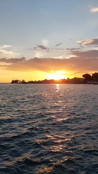 Golden sunset over calm sea water in Biak, Papua, Indonesia, with sunlight reflecting across rippling waves and ships on the distant horizon, ideal for ambient backgrounds.