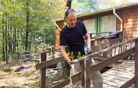 man on an extension ladder using a hammer to nail in new wood siding boards, homeowner maintenance and upkeep, making outdoor repairs on house 