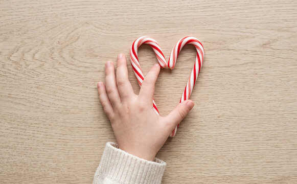 Child hands shaping candy canes into a heart shape on a wooden table representing love and holiday sweetness