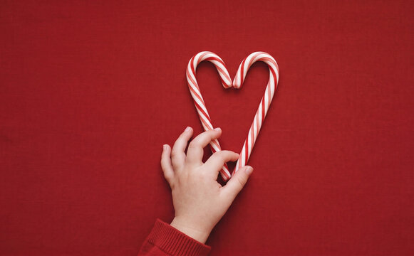 Child hand holding candy canes in heart shape on red background