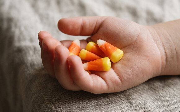 Toddler holding handful of sweet candy corn representing Halloween treats and trick or treating fun