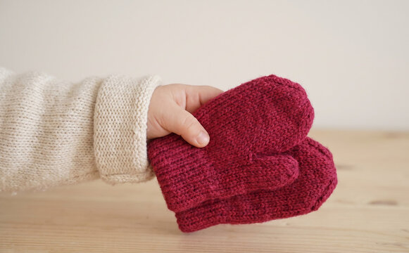 Baby holding red knitted woolen mittens in hand close up for winter clothing concept