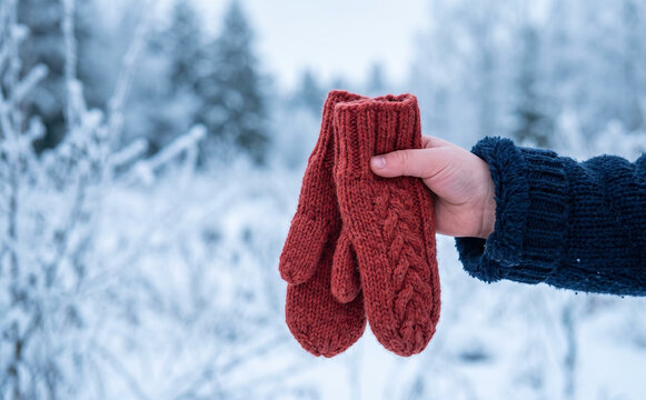 A person holding warm red knitted mittens in a snowy winter forest landscape concept