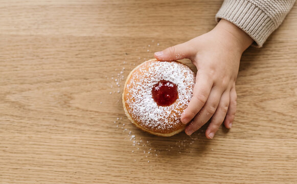 Child touching a delicious powdered jelly donut on a wooden table, top view concept