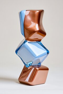 Abstract glossy sculptural object in transparent blue and metallic brown glass, combining futuristic design with modern minimalism