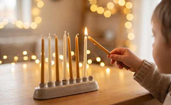 Young boy lighting a menorah with candles for Hanukkah at home, celebrating the Jewish holiday