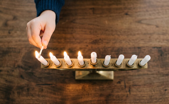 Child lighting Hanukkah menorah candles on wooden table for Jewish holiday celebration