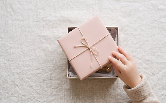 Child opening a pink wrapped present box with a toy inside on a linen table for a birthday concept