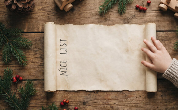 Christmas nice list scroll on rustic wooden table with pine branches and children hand