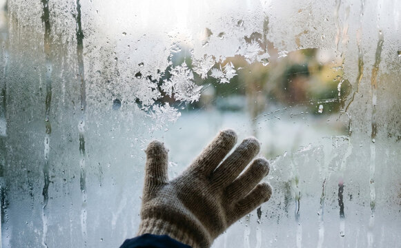 Gloved Hand Touching Frosty Window in Winter Season Representing Cold Weather and Isolation Concept