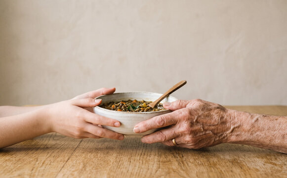 Young and elderly hands holding a bowl of soup representing care, support, and intergenerational connection