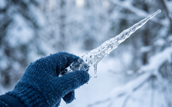 Hand in winter blue glove holding a sharp transparent icicle like a magical ice sword