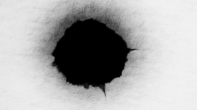 Black ink droplet resting on white textured paper in a minimal overhead scene
