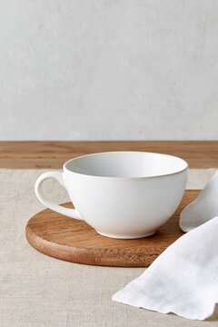 Minimal white ceramic cup on a wooden board with neutral linen and generous copy space