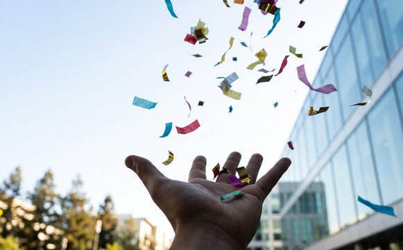 Close up of person throwing colorful confetti in the air celebrating success and achievement outdoors