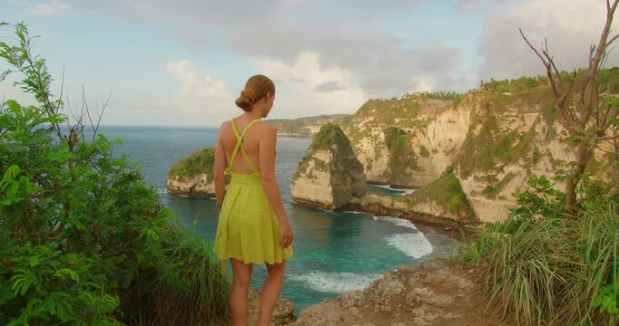 Woman in summer dress looking at ocean view from cliff at Diamond Beach Nusa Penida Bali